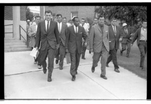 James Meredith walks to class surrounded by protesters, journalists, and armed guards.