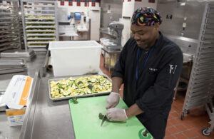 Manager of food services Rodney Rogers slices fresh zucchini in the University of Mississippi Medical Center's main kitchen using a green cutting board designated only for preparation of fruits and vegetables.