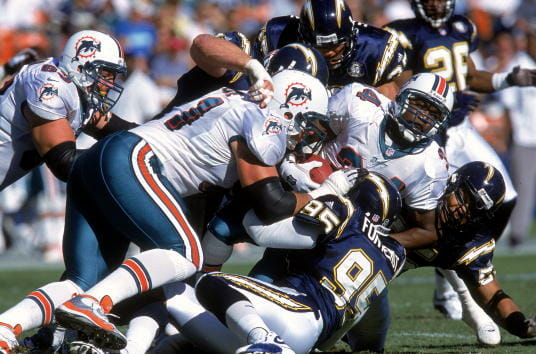 SAN DIEGO - NOVEMBER 12: Thurman Thomas #34 of the Miami Dolphins carries the ball as he is tackled by Todd Wade #71 and Albert Fontenot #95 of the San Diego Chargers on November 12, 2000 at Qualcomm Stadium in San Diego, California. The Dolphins defeated the Chargers 17-7. (Photo by Stephen Dunn/Getty Images)
