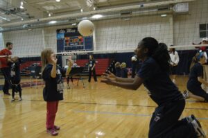 Junior Marie-Pierre Bakima helps the girls practice setting a volleyball.