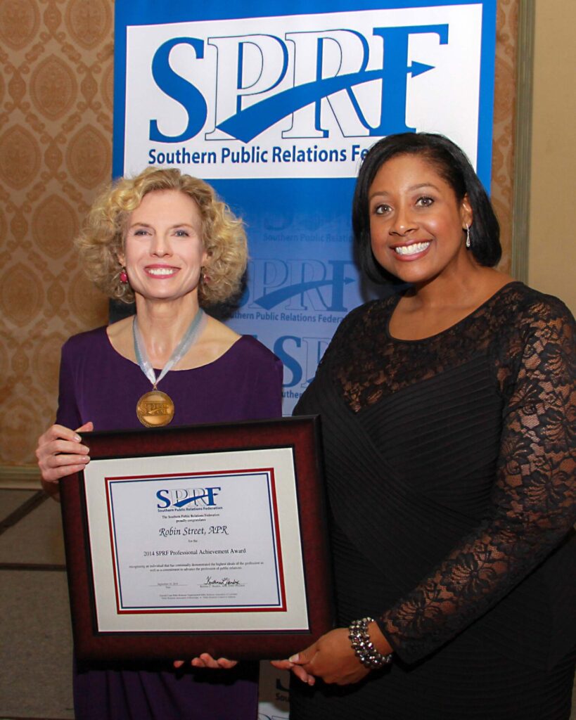 Robin Street, a lecturer in the Meek School of Journalism and New Media, received the Professional Achievement Award, the highest professional honor given for lifetime achievement in the profession, from the Southern Public Relations Federation. SPRF president Kristina Hendrix (right) presented Street with a framed certificate and medallion. As the winner of Mississippi’s Professional Award, Street then competed with nominees from several other states.  (Photo credit: Leo Ridge, Big Top Photo Booth) 