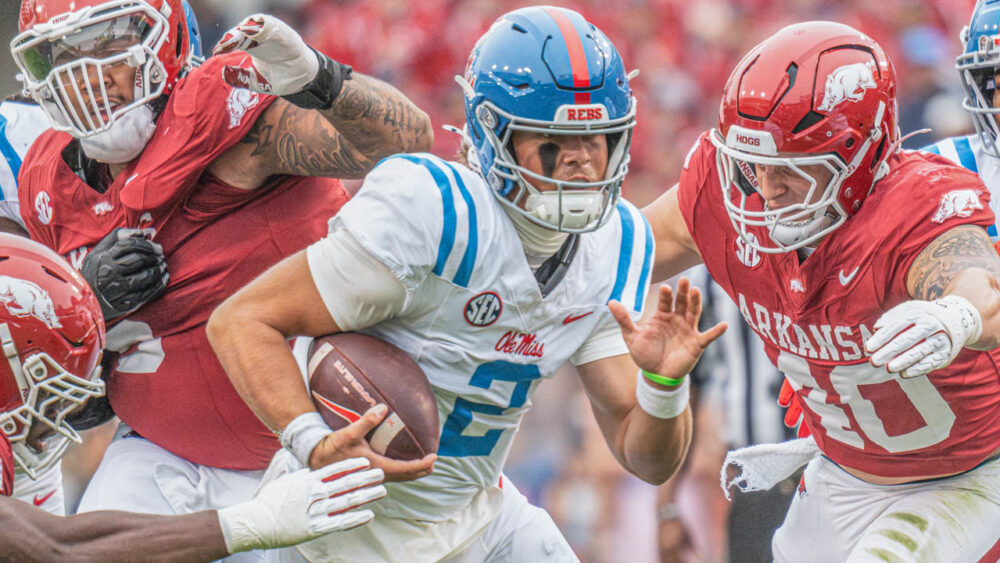 Rebels quarterback Jaxson Dart runs through Arkansas defenders Larry Worth and Landon Jackson