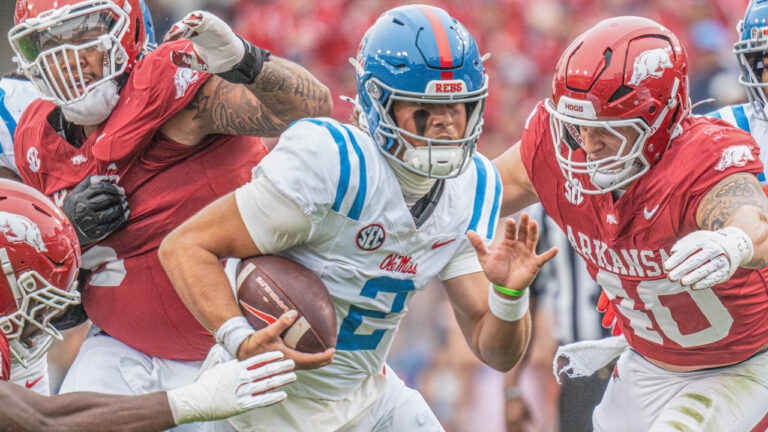 Rebels quarterback Jaxson Dart runs through Arkansas defenders Larry Worth and Landon Jackson